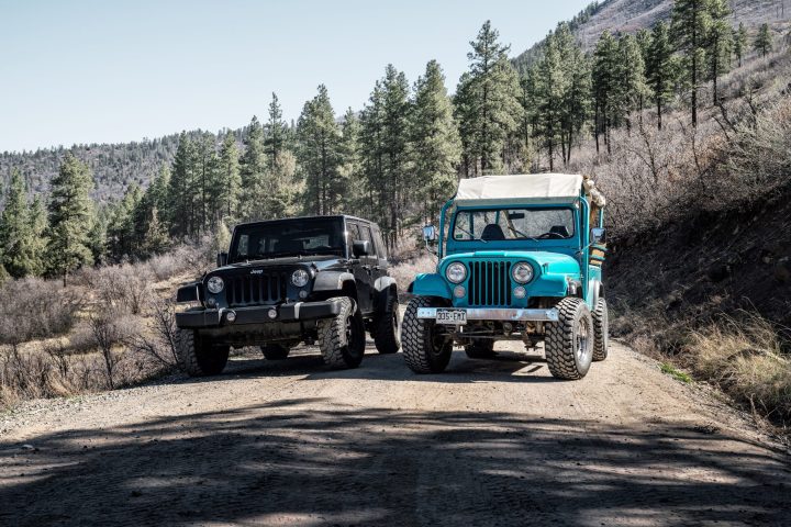 A black Jeep and a turquoise Jeep parked next to each other on a forest road in Colorado