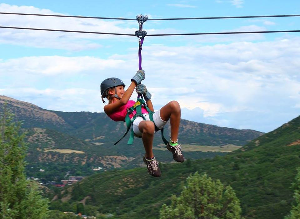 Durango things to do A man soars above the ground on a zip line with beautiful forests and mountains in the background