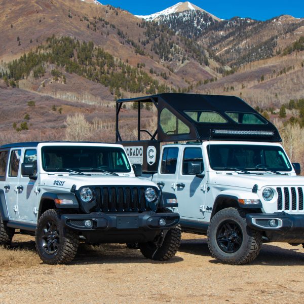 Two white jeeps are parked next to each other in front of a mountain