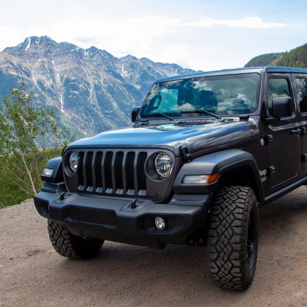 A black Jeep is parked on a forest road in the Colorado wilderness with a large mountain in the background