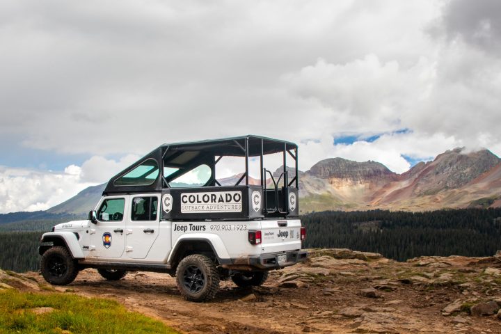 A white Jeep Gladiator rig is parked in front of a beautiful vista and mountains