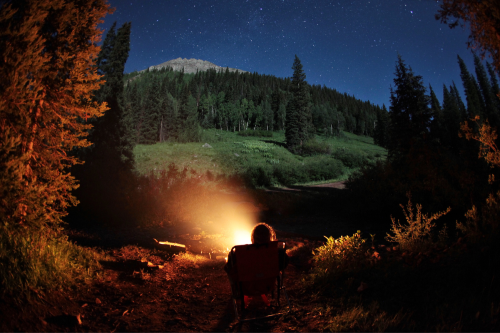 a camper sits at a campfire with a mountain in the background