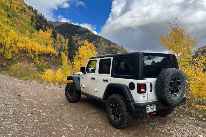 White SUV on a mountain road with autumn trees and clouds in the background.