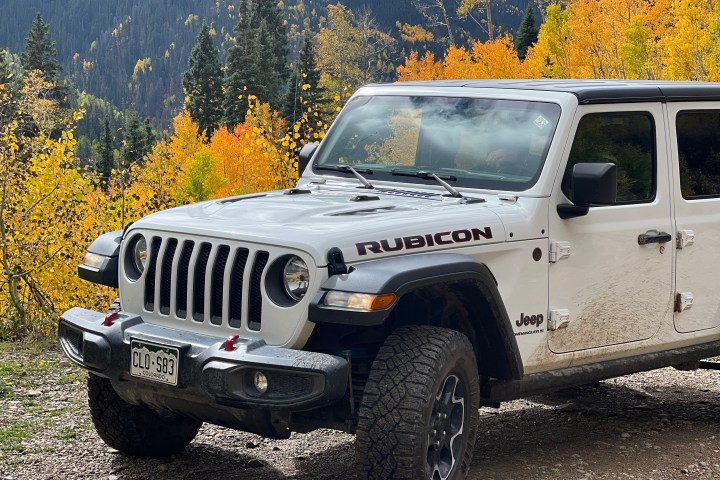 White Jeep Rubicon parked on a mountain road with autumn trees in the background.